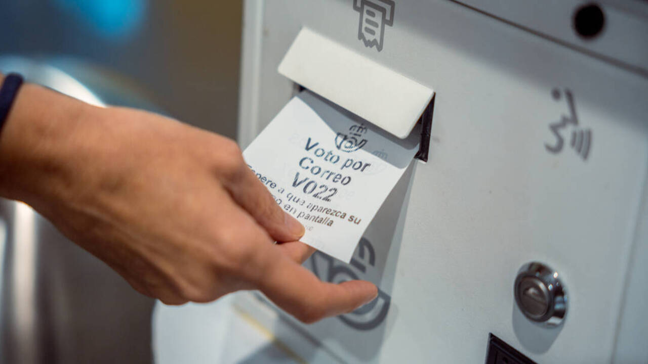 Un ciudadano toma el ticket de su turno de espera en una oficina de Correos para tramitar el voto por correo