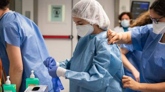 Una enfermera ayudando a una compañera a colocarse la bata en Urgencias