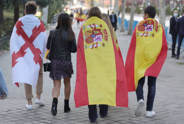 Un joven con la bandera de la Cruz de Borgoña (i) y otros tapados con la bandera de España se dirigen acto solemne de homenaje a la bandera nacional y desfile militar en el Día de la Hispanidad, a 12 de octubre de 2021, en Madrid