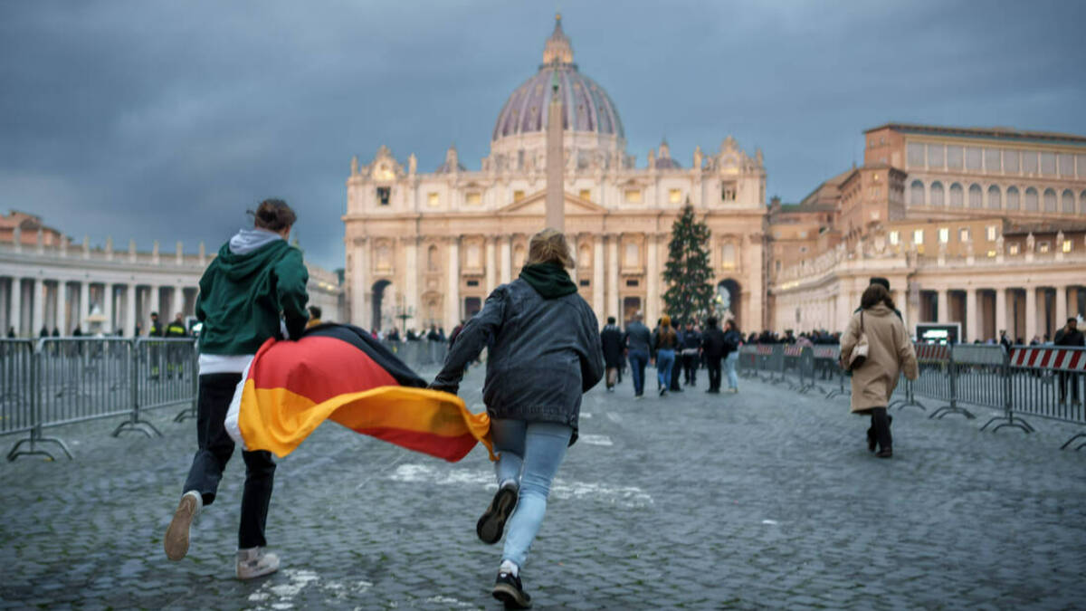 Dos fieles con la bandera de Alemania corren hacia la cola para despedir a Benedicto XVI