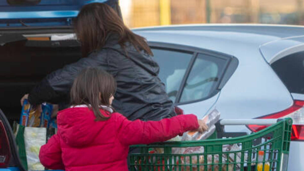 Una mujer y una niña meten la compra en el maletero del coche al salir de un supermercado.