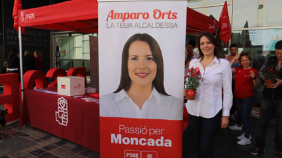 Imagen de Amparo Orts con las plantas repartidas a los vecinos con el logo del PSOE en la maceta. 