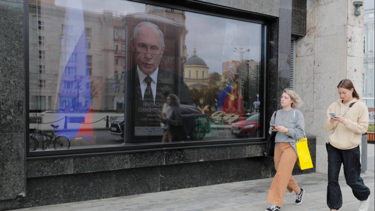 Dos mujeres rusas pasan delante de una pantalla en la que aparece el presidente Putin.