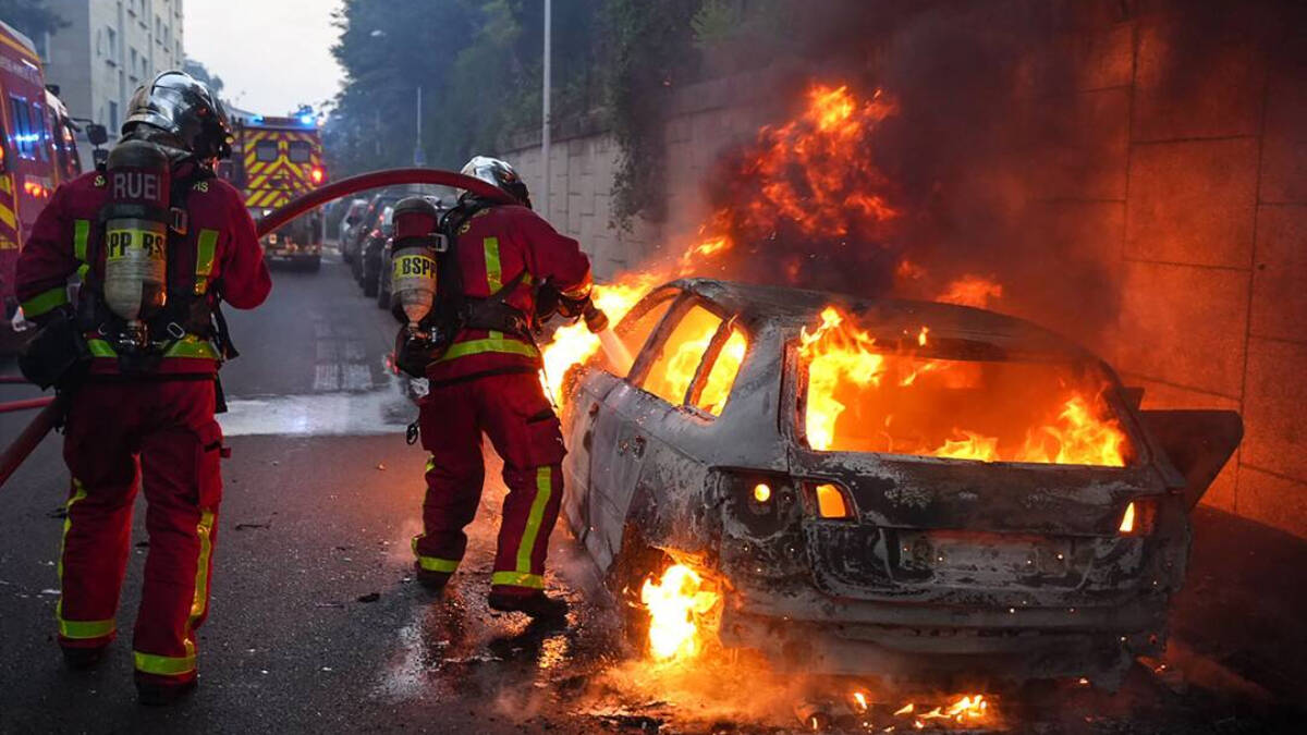 Unos bomberos apagan uno de los coches incendiados tras la noche de disturbios en Nanterre.