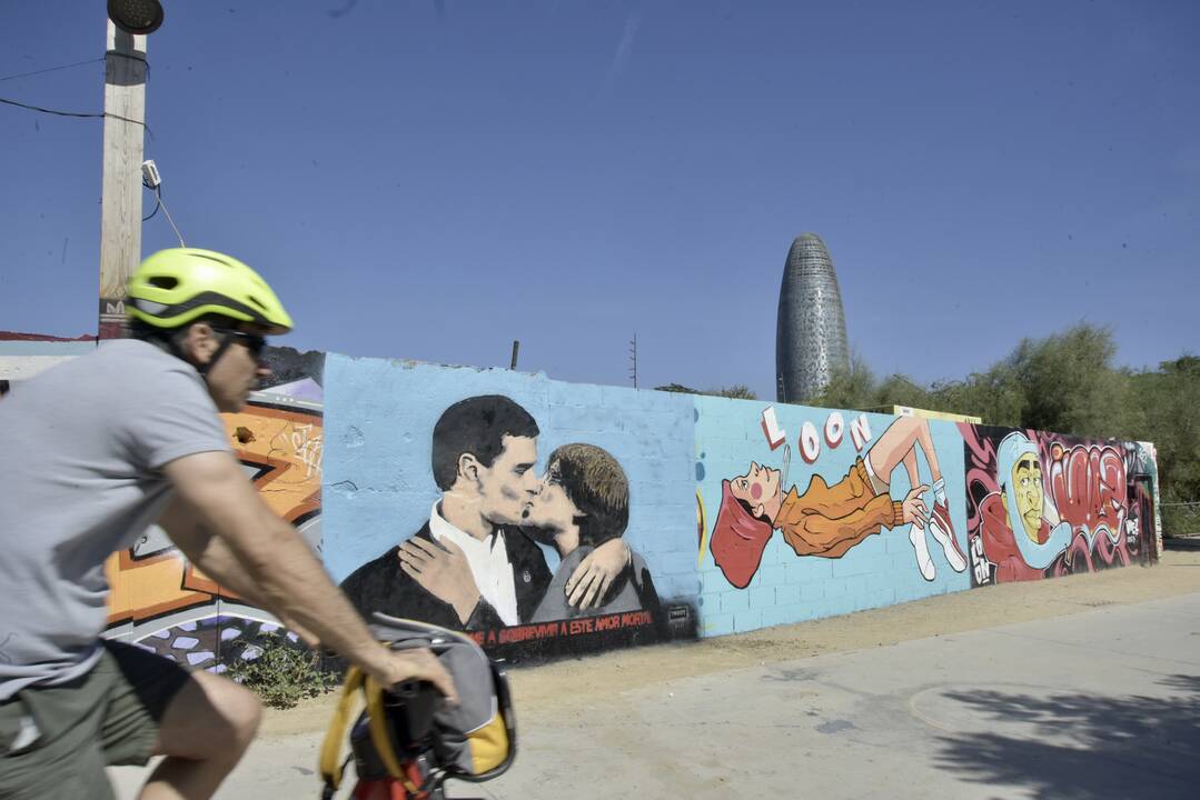 Un ciclista pasa al lado de la pintura del presidente Pedro Sánchez y al expresidente de la Generalitat y eurodiputado de Junts, Carles Puigdemont, dándose un beso en el mural del artista urbano TVBoy