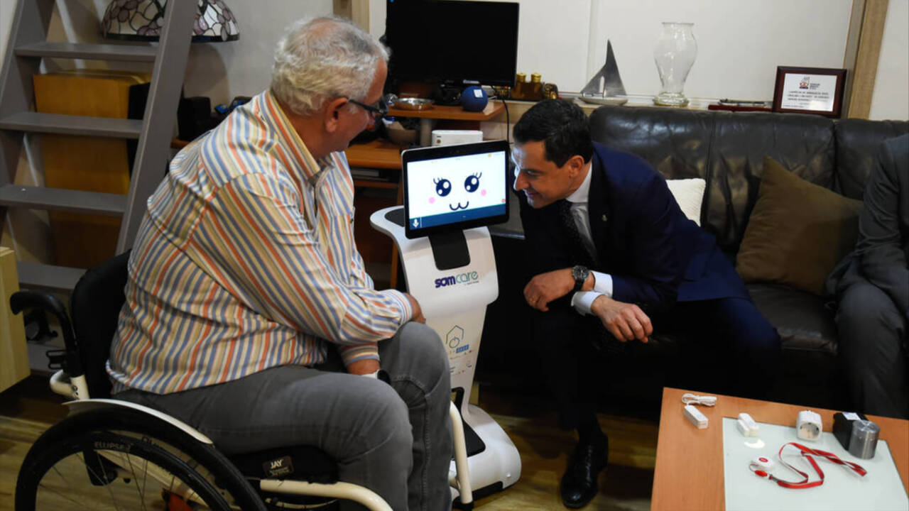 El presidente de la Junta de Andalucía, Juanma Moreno, entrega a una persona con discapacidad un robot del proyecto Vivir en casa.